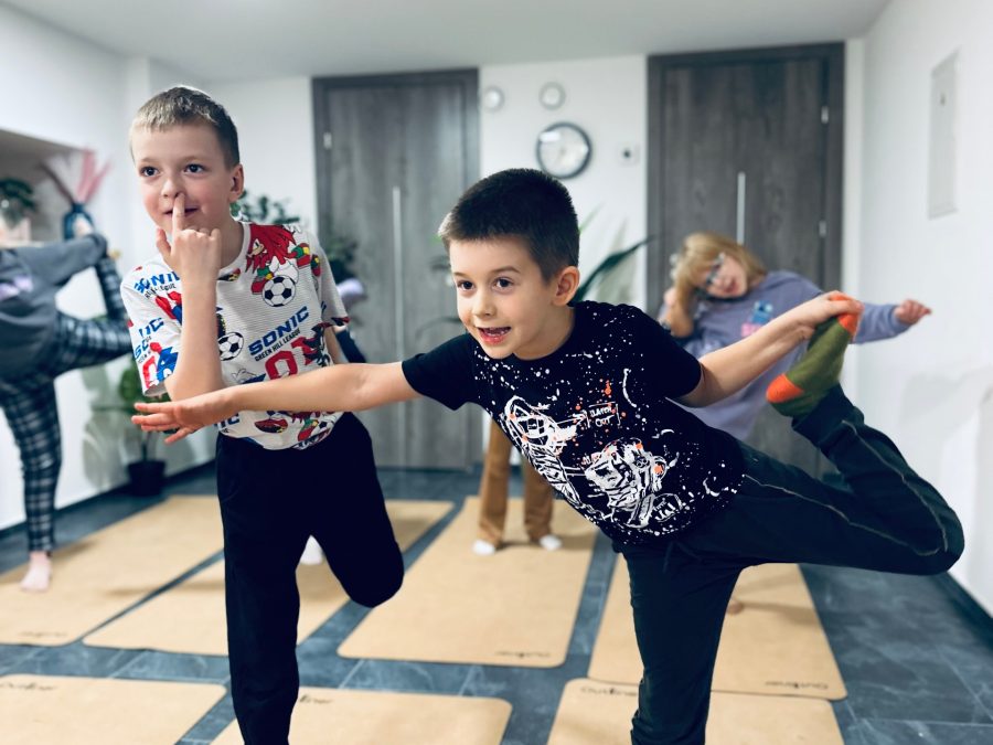 Du berniukai stovi medžio pozoje vaikų jogos užsiėmime progimnazijos salėje