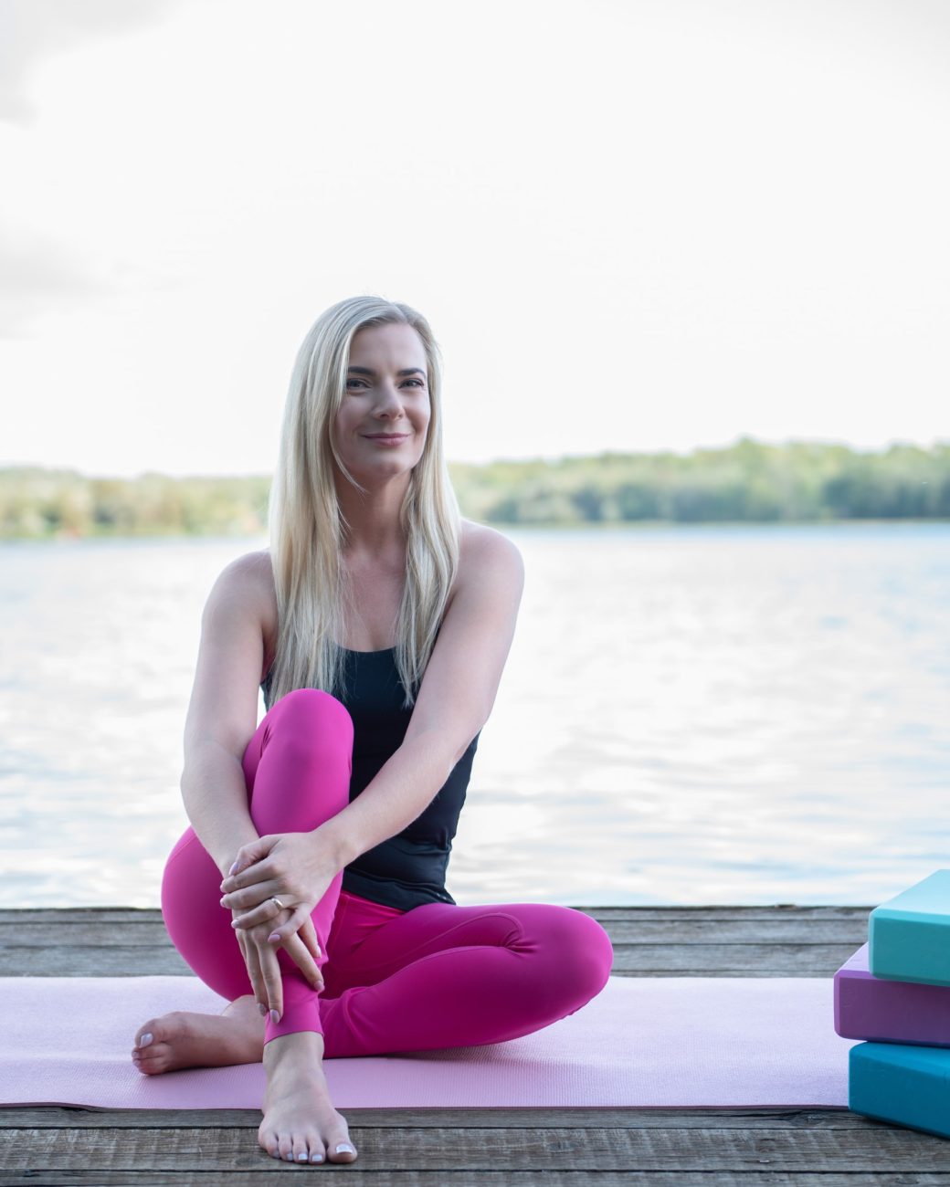 Pueri Yoga vaikų jogos mokytoja sėdi ant kilimėlio prie ežero