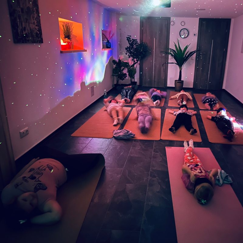 Tamsi salė su jogos kilimėliais ir neoniniu apšvietimu meditacijos metu